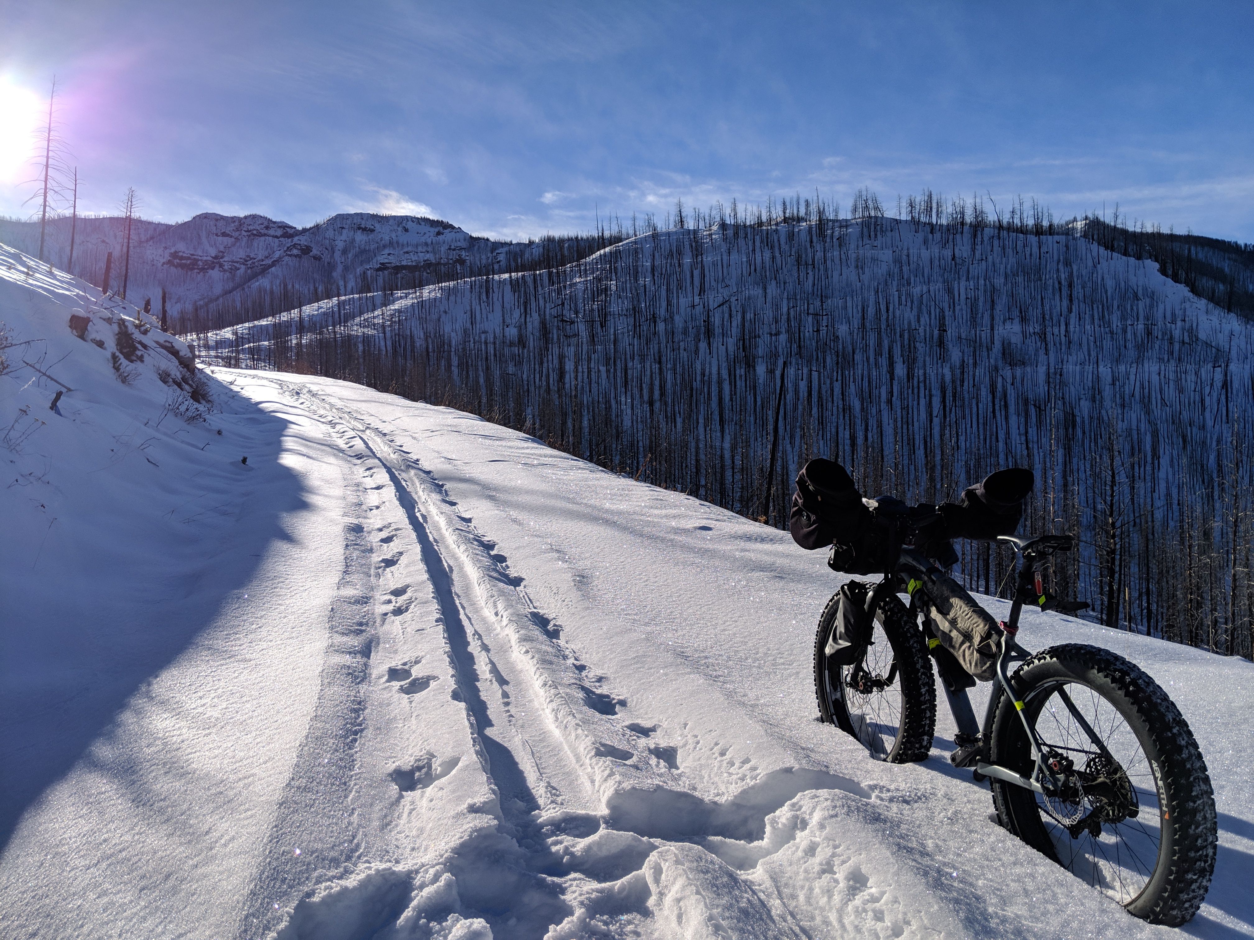Mountain bike with bar mitts and framebag in deep snow in the sun on a mountain road